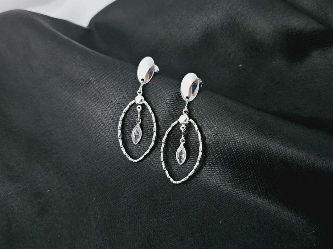 Brinco com base oval lisa e circulo trabalhado vazado com zirconia losango pendurado ao centro banhada a prata