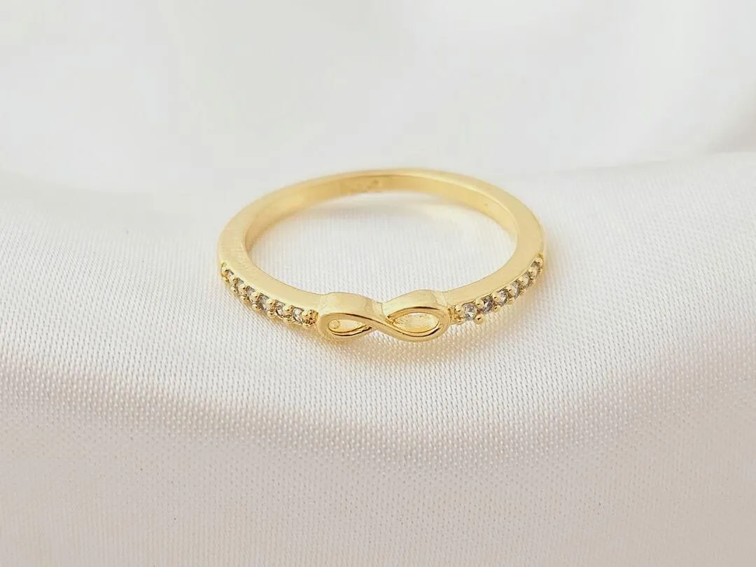 Anel com infinito no centro e micro zirconias ao redor, banhado a ouro, medindo 0,2cm de espessura