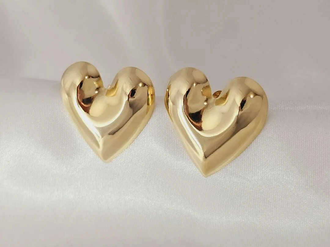 Brinco de coração alto relevo, banhado a ouro, medindo 2,5cm x 2,5cm.